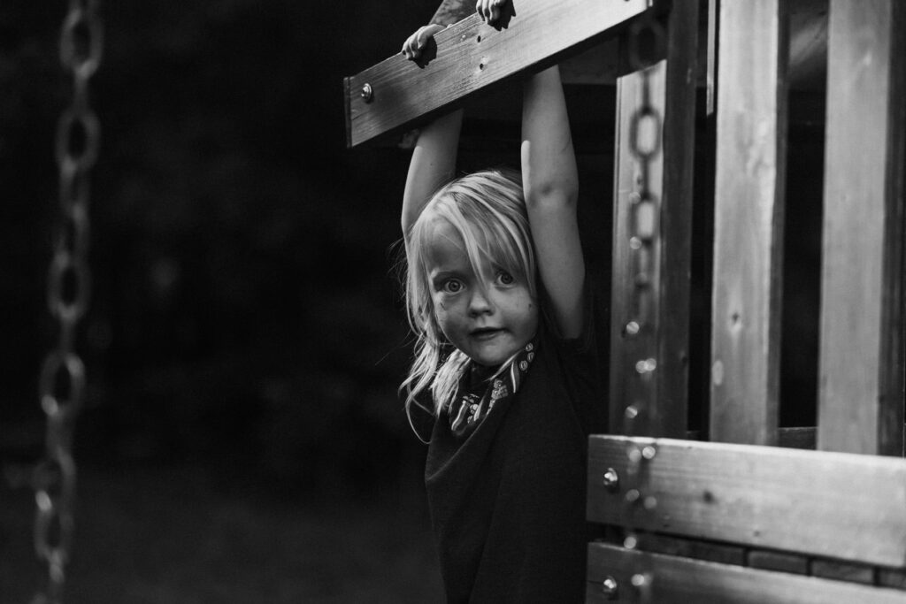 A young child hanging on a playset, candid black and white