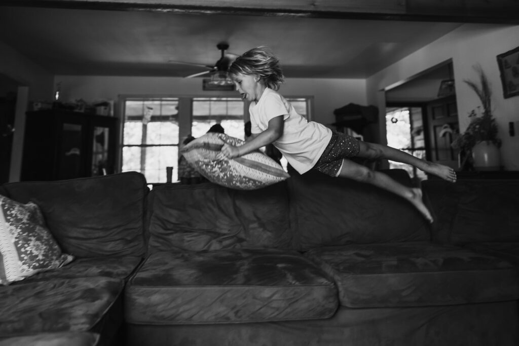 kid flying through the air over his couch with a pillow