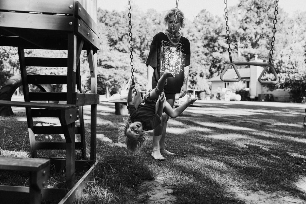 a child hanging from a swing while his mother stands behind