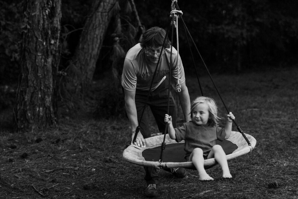 father pushing his young child on a swing, candid