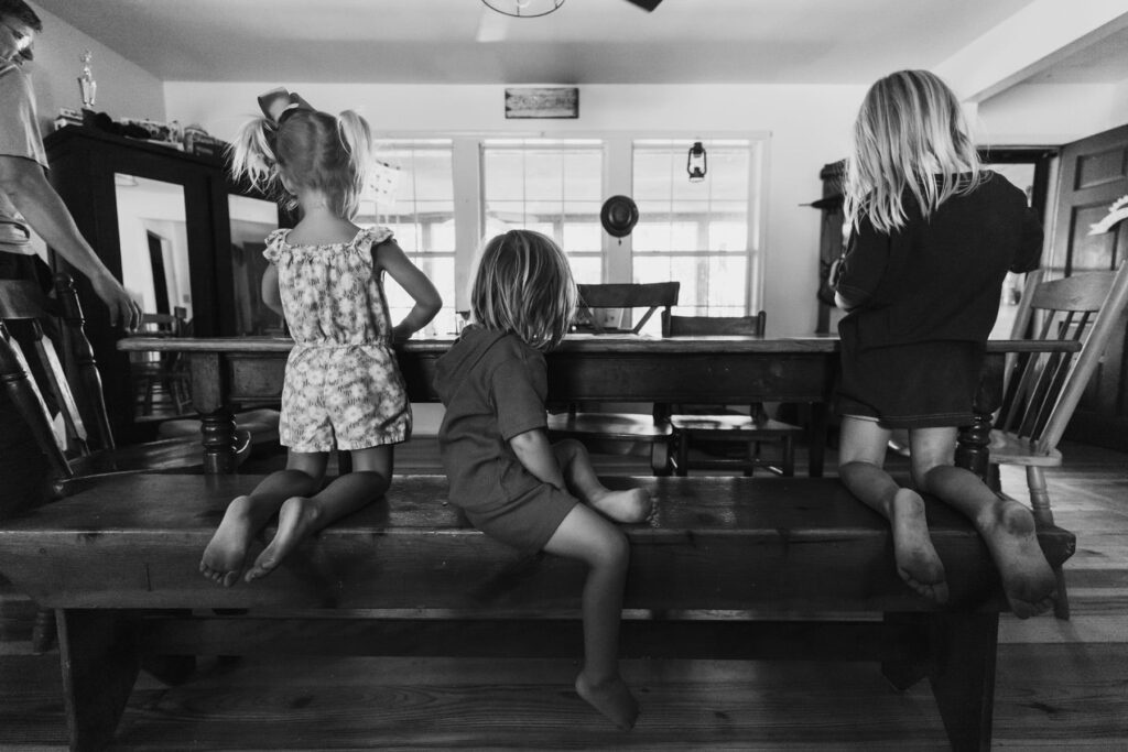 3 young children at a table, candid from behind